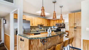 A modern kitchen with wooden cabinets, a granite countertop, and a bar area with stools. - 3-bedroom Phoenix Cabin with cool AC for relaxing stay (Phoenix)