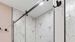 Une cabine de douche moderne avec des portes en verre aux motifs géométriques et un sol carrelé en forme d’hexagone.
