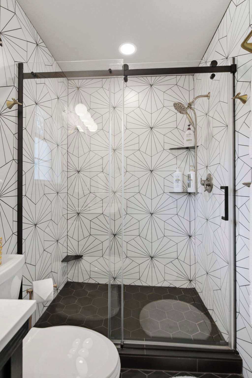 Ein modernes Badezimmer mit geometrischen Wandmustern, einer Glasdusche und einer weißen Toilette.