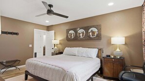 Une chambre à coucher avec un lit, des lampes de chevet, un ventilateur de plafond et un miroir fixé au mur.
