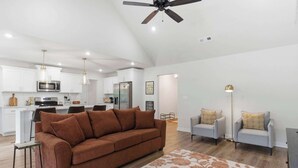A modern living room with a brown sofa, two grey armchairs, a patterned rug, and a ceiling fan. - May Way | Trails, Golf, Hiking & Relaxation (Bella Vista)