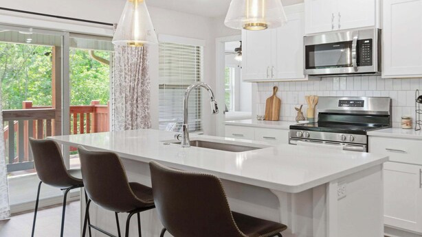 A modern kitchen with a large island, white cabinetry, stainless steel appliances, and pendant lighting. - May Way | Trails, Golf, Hiking & Relaxation (Bella Vista)