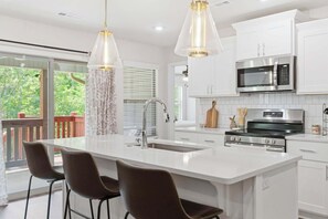A modern kitchen with a large island, white cabinetry, stainless steel appliances, and pendant lighting.