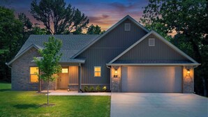 A two-story house with a garage, a small tree in the front yard, and a driveway leading to the garage. - May Way | Trails, Golf, Hiking & Relaxation (Bella Vista)