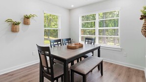 A dining area with a table, chairs, and two windows with blinds. - May Way | Trails, Golf, Hiking & Relaxation (Bella Vista)