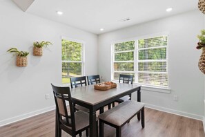 A dining area with a table, chairs, and two windows with blinds.
