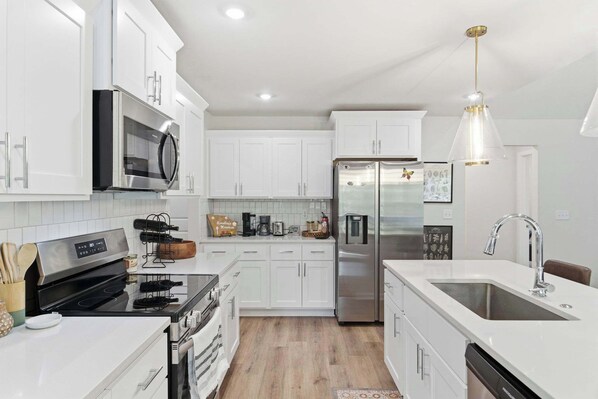 A modern kitchen with white cabinetry, stainless steel appliances, and a pendant light.