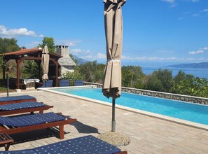 Ein Poolbereich mit Liegestühlen, einer Pergola und Blick auf das Meer.