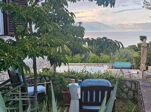 A patio with outdoor furniture, a view of the sea, and a stone wall. - Apartments Valerija (Rasa)