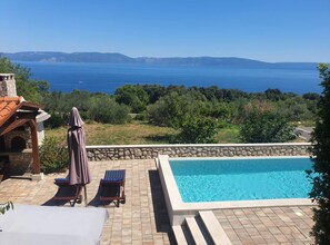 A swimming pool with a stone wall, lounge chairs, and a stone oven structure. - Apartments Valerija (Rasa)