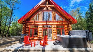 Eine Blockhütte mit einer großen Haustür, zwei roten Stühlen, einem Whirlpool und einem Grill.