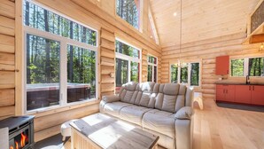 Ein Blockhaus-Interieur mit einer Couch, einem Tisch, einem Kamin und großen Fenstern.