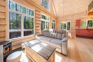 A log cabin interior with a sofa, a table, a fireplace, and large windows.