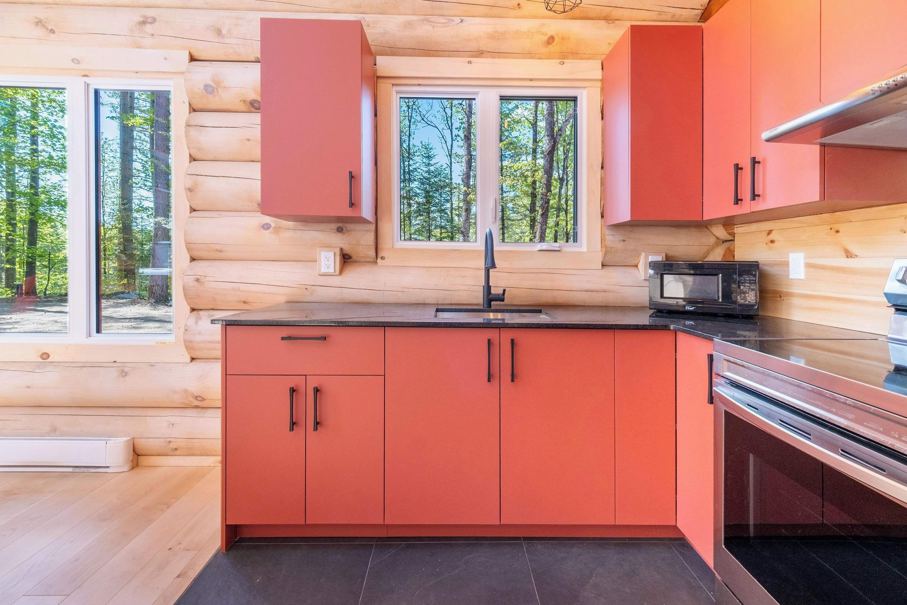 A modern kitchen with wooden log walls, red cabinets, a black countertop, and a microwave.