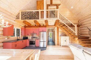 A log cabin interior with a kitchen, dining area, and a staircase.