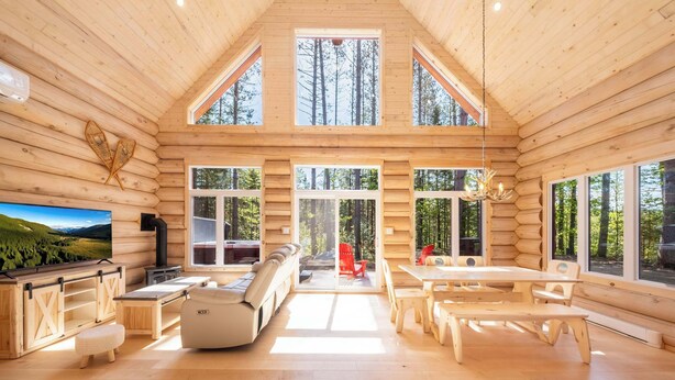 Ein Blockhaus-Interieur mit einem großen Fernseher, Holzmöbeln und großen Fenstern.
