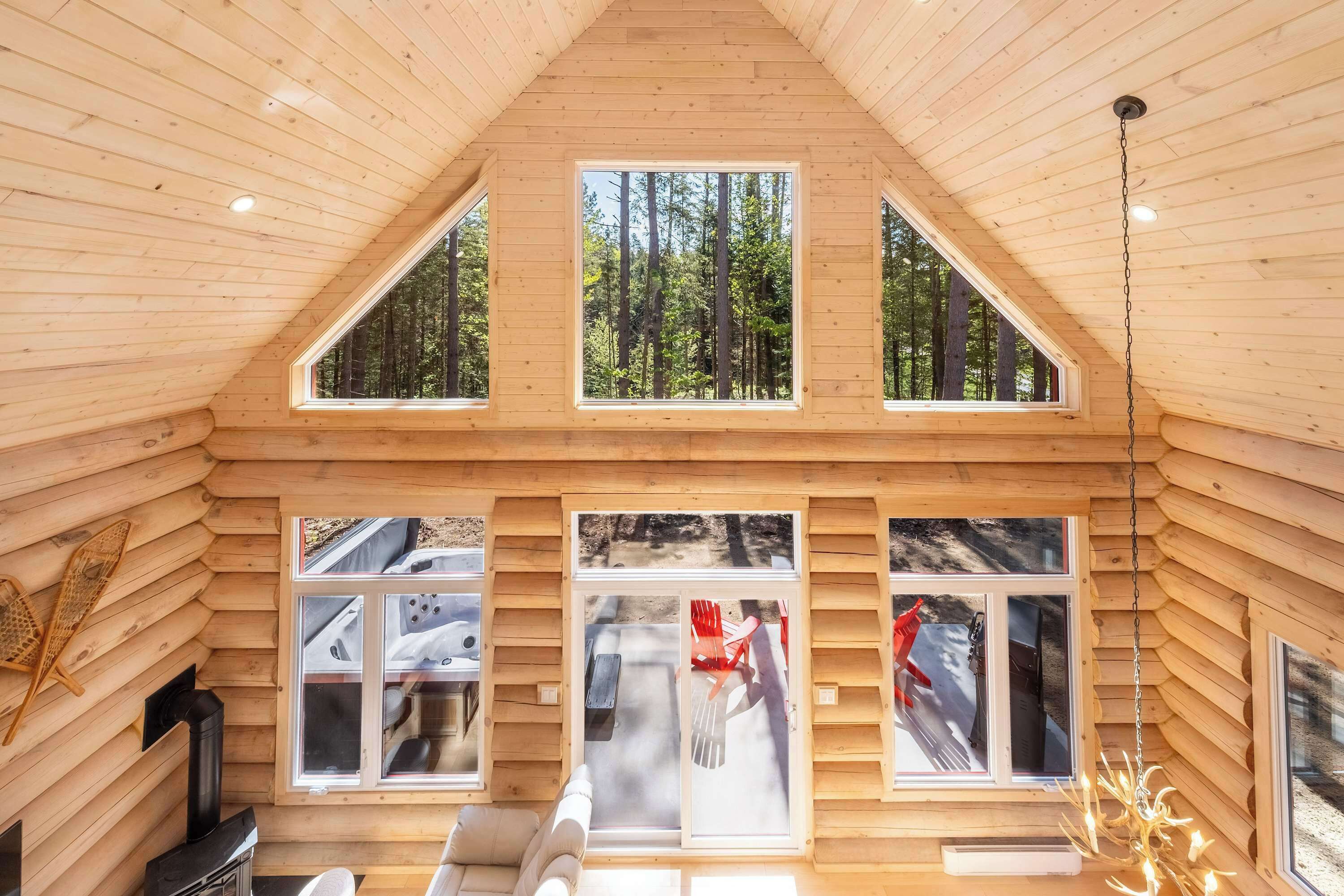 L’intérieur d’une cabane en rondins, avec un plafond en pente, de grandes fenêtres, une cheminée et un coin salon confortable.