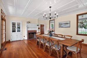 Ein Esszimmer mit Holztisch und -stühlen, einer Kristallleuchtre, einem Kamin und Blick ins Freie.