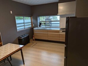 A kitchen with wooden cabinets, a black refrigerator, and a window with blinds. - Yuki Niwa (Myoko)
