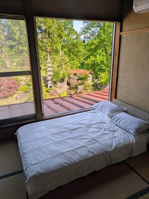 A room with a bed, large windows, and a view of a temple and greenery. - Yuki Niwa (Myoko)