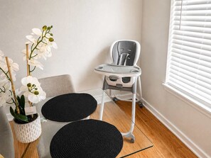 A room with a white wall, a window with blinds, a grey baby rocker, a white potted orchid, and two black circular rugs. - Pet-Friendly 2BR Dallas Retreat - Sleeps 6 (Dallas)