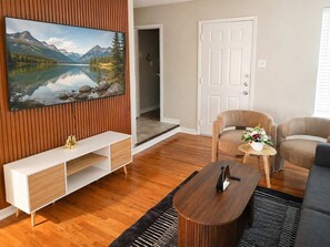 A modern living room with a wooden floor, a mounted TV, a sofa, a coffee table, and a door leading to another room. - Pet-Friendly 2BR Dallas Retreat - Sleeps 6 (Dallas)
