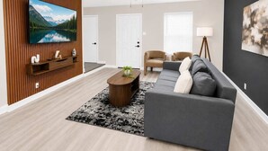 Ett modernt vardagsrum med en platt-TV, en takfläkt, en soffa, ett soffbord och en lampa.