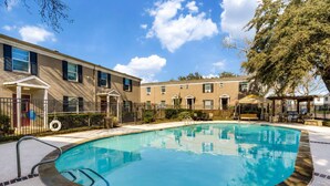A swimming pool with a tiled deck, surrounded by a fence, and adjacent to a building with multiple windows and a covered patio area. - 2BR Dallas Townhome - Pool, King Bed & Parking (Dallas)