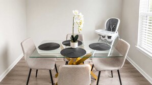 A dining area with a glass table, four chairs, a white orchid, and a baby high chair. - 2BR Dallas Townhome - Pool, King Bed & Parking (Dallas)