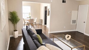 A modern living room with a dark-colored sofa, a glass coffee table, and a potted plant. - 2BR Dallas Townhome - Pool, King Bed & Parking (Dallas)