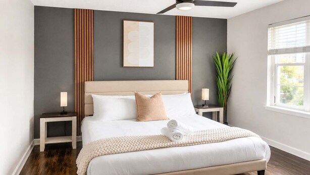A modern bedroom with a bed, bedside tables, a ceiling fan, and a large window. - 2BR Dallas Townhome - Pool, King Bed & Parking (Dallas)