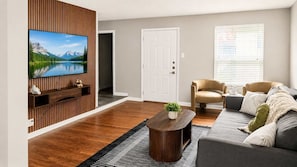 A modern living room with a flat-screen TV, a sofa, a coffee table, and a wooden accent wall. - 2BR Near Medical District - Pool & Parking (Dallas)