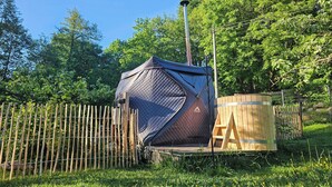 A tent with a metal pole, a wooden structure, and a fence in a green, grassy area.
