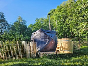A tent with a metal pole, a wooden structure, and a fence in a green, grassy area.