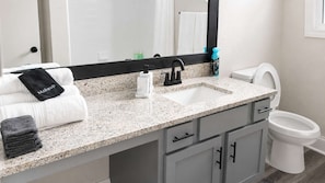 Une salle de bain avec un comptoir en granit, un lavabo, des toilettes et un miroir.