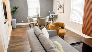 Ein modernes Wohnzimmer mit einem grauen Sofa, einem gelben Sessel, einem Esstisch mit Stühlen und einer Topfpflanze.
