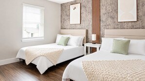Ein Hotelzimmer mit zwei Betten, einem kleinen Tisch und einem Fenster mit Jalousien.