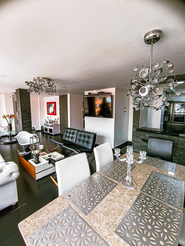 A modern living room with a sofa, a dining table with a patterned table runner, a chandelier, and a flat-screen TV mounted on the wall. - Beautiful and Spacious Apartment in Chapinero Bogota DC (Bogotá, D.C.)