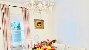 A dining room with a white table, chairs, a chandelier, and a bowl of fruit.