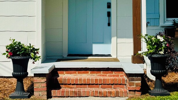 A house with a blue front door, a brick entrance, and two black lantern-style lights.