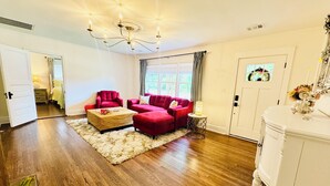 A spacious room with hardwood flooring, a red sofa set, a white cabinet, and a chandelier.