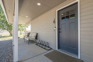 A house entrance with a gray door, a covered porch, a chair, and a bike rack. - NEW! Horsethief Hideaway Near Trails (Loma)