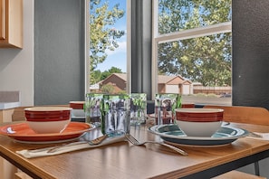 A dining table set with bowls, glasses, and cutlery, positioned near a window with a view of houses and trees. - NEW! Horsethief Hideaway Near Trails (Loma)