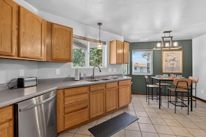 A kitchen with wooden cabinets, a stainless steel dishwasher, a sink, and a dining area with chairs and a table. - NEW! Horsethief Hideaway Near Trails (Loma)