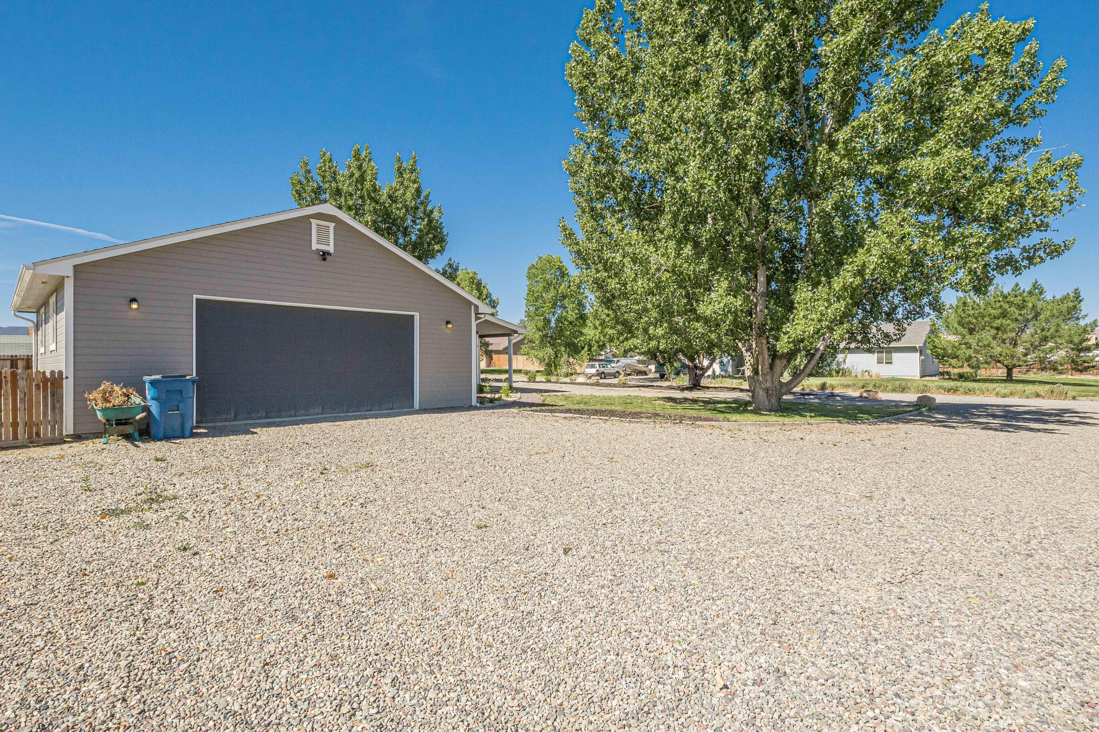 A single-story building with a garage, gravel driveway, and a large tree in front.