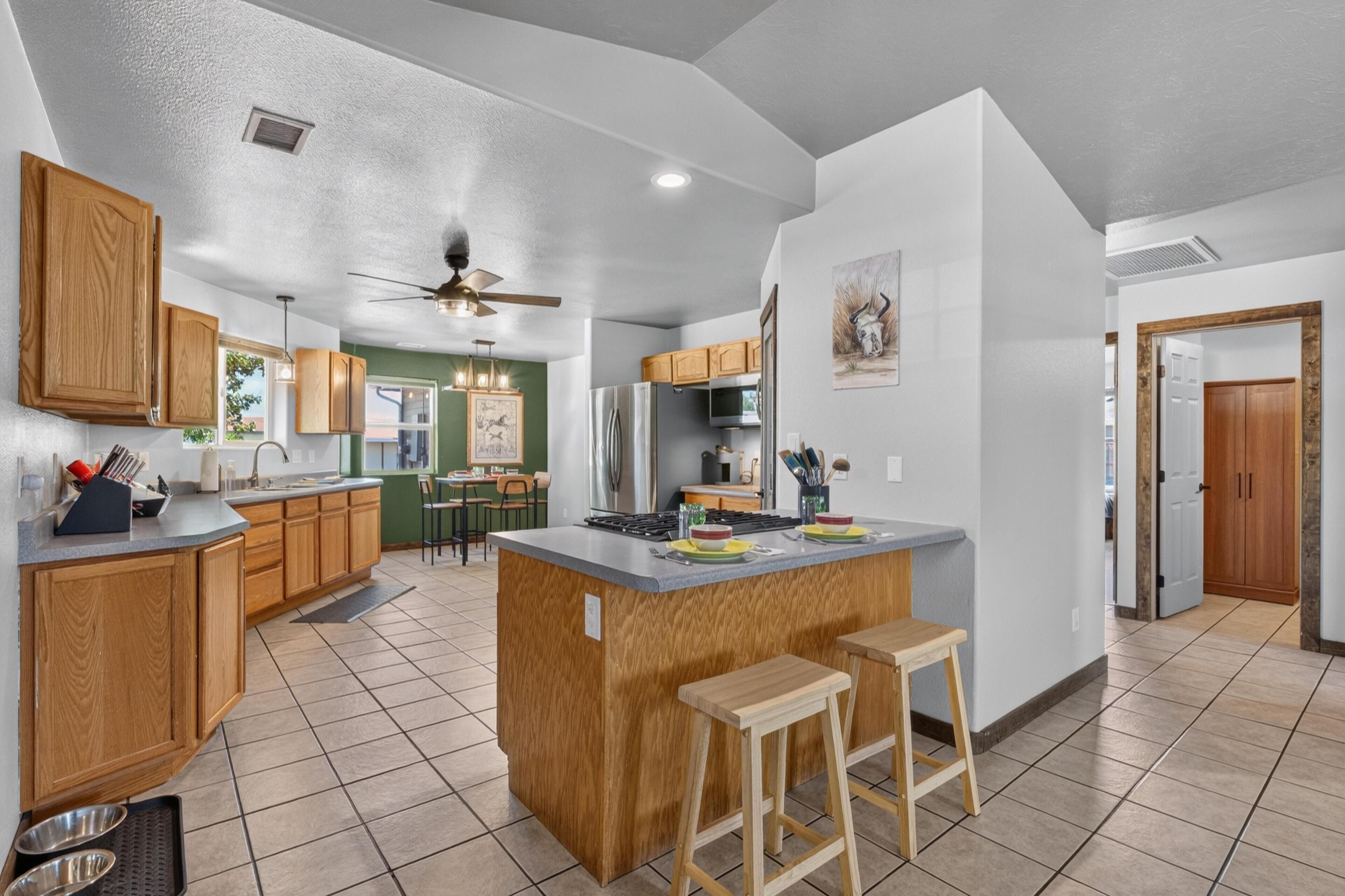 A kitchen with wooden cabinets, a central island, stools, a ceiling fan, and a dining area with chairs and a table.