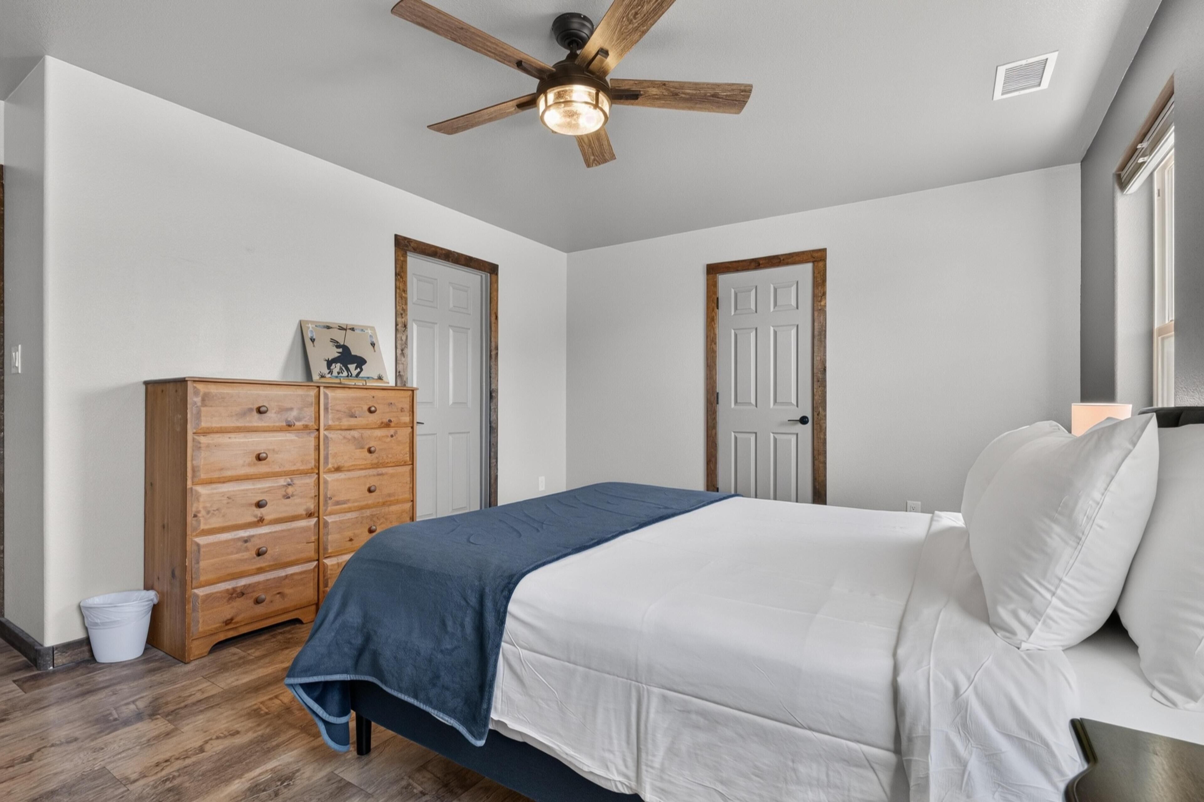A bedroom with a bed, wooden dresser, ceiling fan, and two doors.