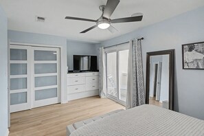 Ein Schlafzimmer mit Bett, Deckenventilator, Fernseher, Kleiderschrank und einer Schiebetür zu einem Balkon.