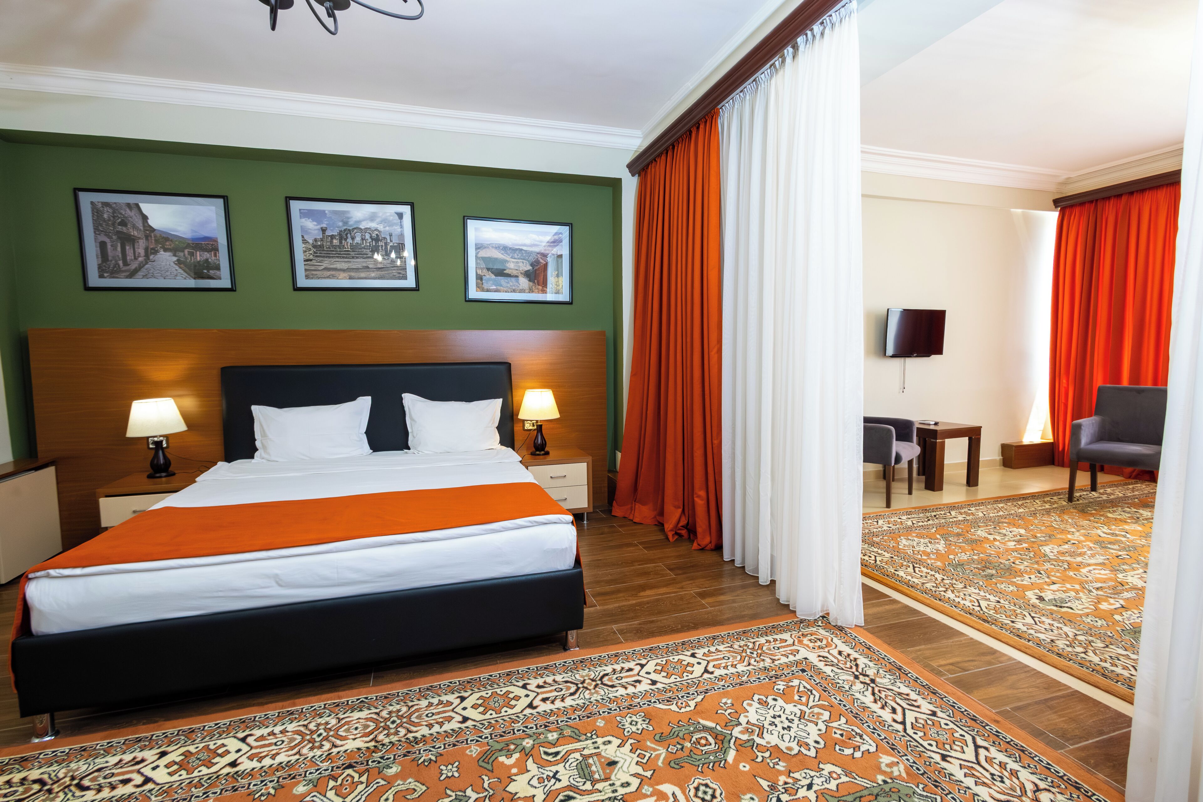 A hotel room with a large bed, two bedside lamps, a flat-screen TV, a wooden headboard, and a patterned rug.
