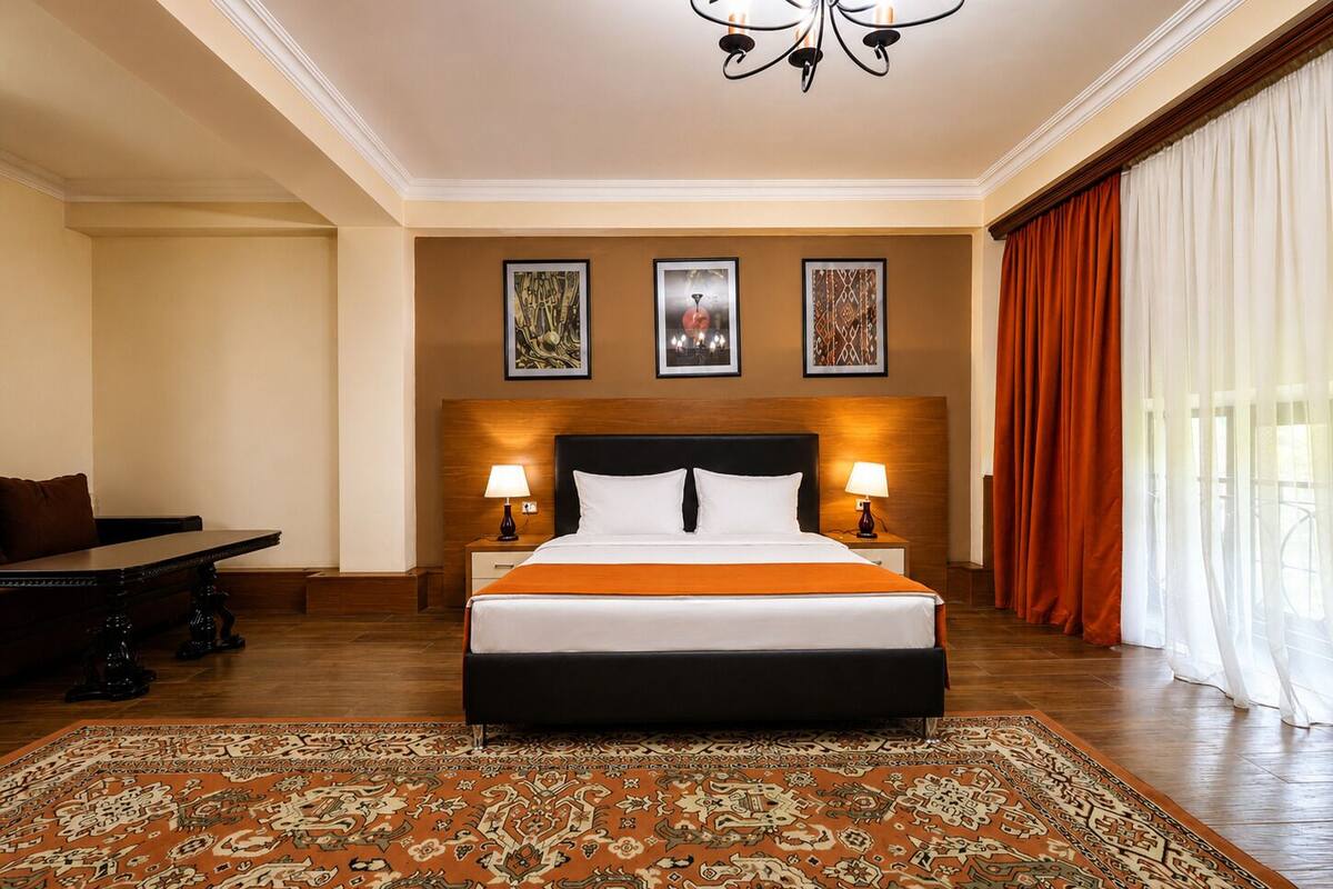 Habitación de hotel con una cama grande, dos lámparas de noche, una araña y una alfombra estampada, además de vistas al exterior.